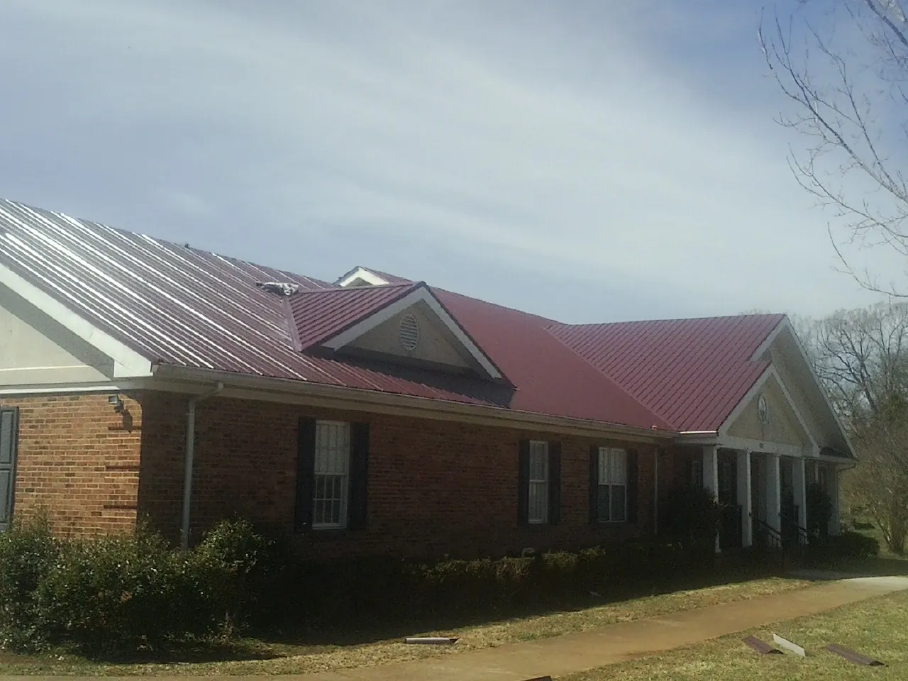 Red metal roof with gabled entries on a long brick building, from a Hail Damage Roof Repair job in Deer Lodge