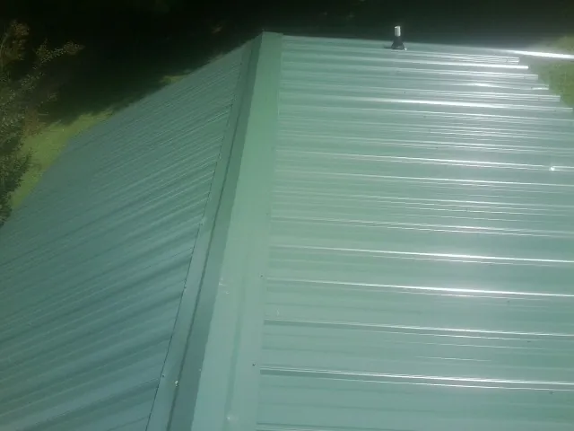 New green metal panels meeting at the ridge of a roof — Flat Roof Repair work by our crew in Deer Lodge